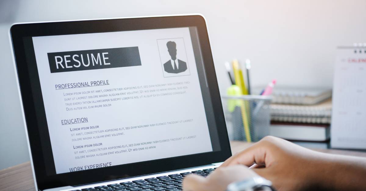 A person's hands rest on a laptop with the screen showing a professional resume template including profile and education.